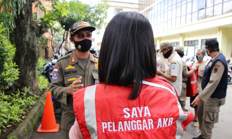 Seorang warga yang kedapatan tidak menggunakan masker saat beraktivitas di luar mendapat hukuman dari para petugas yang sedang melaksanakan razia protokol kesehatan.