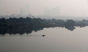 Seorang warga mendayung perahu ketika bangunan-bangunan yang diselimuti kabut asap terlihat di latar belakang di pinggiran Delhi, India, 15 November 2021. (ANTARA/Reuters/as)