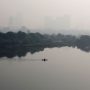 Seorang warga mendayung perahu ketika bangunan-bangunan yang diselimuti kabut asap terlihat di latar belakang di pinggiran Delhi, India, 15 November 2021. (ANTARA/Reuters/as)