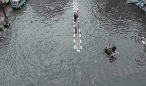 KOLAM RETENSI JADI SOLUSI: Pengendara roda dua tampak terjebak banjir dan harus mendorong kendaraanya untuk menghindari banjir. (KHOLID/JABAREKSPRES)