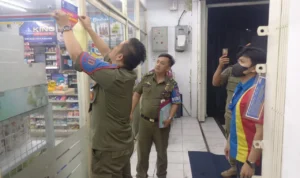 Kepala Bidang Gakda Satpo PP dan Damkar Kota Cimahi Ranto Sitanggang memasang stiker di bagian depan toko modern yang melanggar jam operasional.