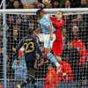Kiper Real Madrid, Andriy Lunin (merah), saat menghalau bola di udara melawan Manchester City, Kamis (18/4).