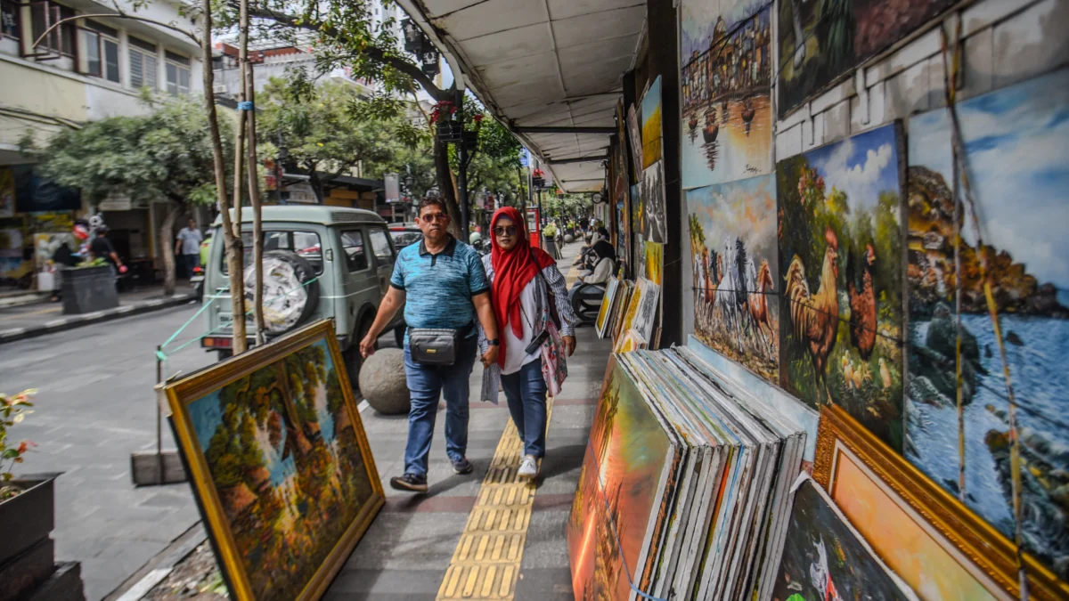 Warga berjalan di dekat lukisan yang di jual dikawasan Braga, Kota Bandung, Kamis (23/1). Foto: Dimas Rachmatsyah / Jabar Ekspres
