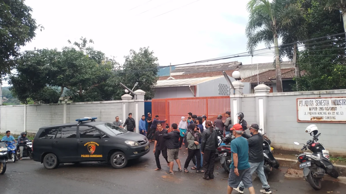 Sejumlah warga berada di depan pabrik dan satu unit mobil Reskrim Polres Sumedang tengah memasuki area PT Adira Semesta Industry, untuk menyelidiki dugaan tiga pekerja yang diduga meninggal saat membersihkan sumur limbah. (Yanuar/Jabar Ekspres)