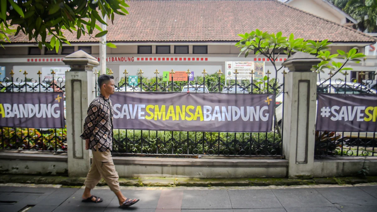 Seorang warga berjalan di dekat spanduk bertuliskan "SAVESMANSABANDUNG" di depan SMA Negeri 1, Kota Bandung, Jum'at (21/3). Foto: Dimas Rachmatsyah / Jabar Ekspres