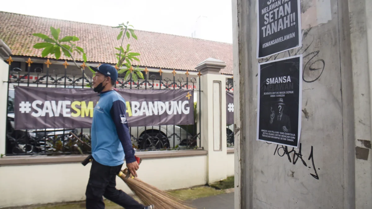 Petugas kebersihan berjalan di samping poster perlawanan di depan SMA Negeri 1, Kota Bandung, Senin (21/4). Foto: Dimas Rachmatsyah / Jabar Ekspres