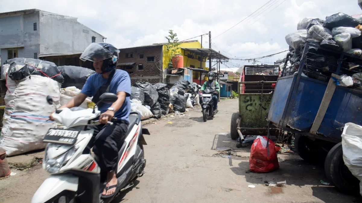 Pengendara motor melintas di samping tumpukan sampah di TPS di Kota Bandung. Foto: Dimas Rachmatsyah / Jabar Ekspres