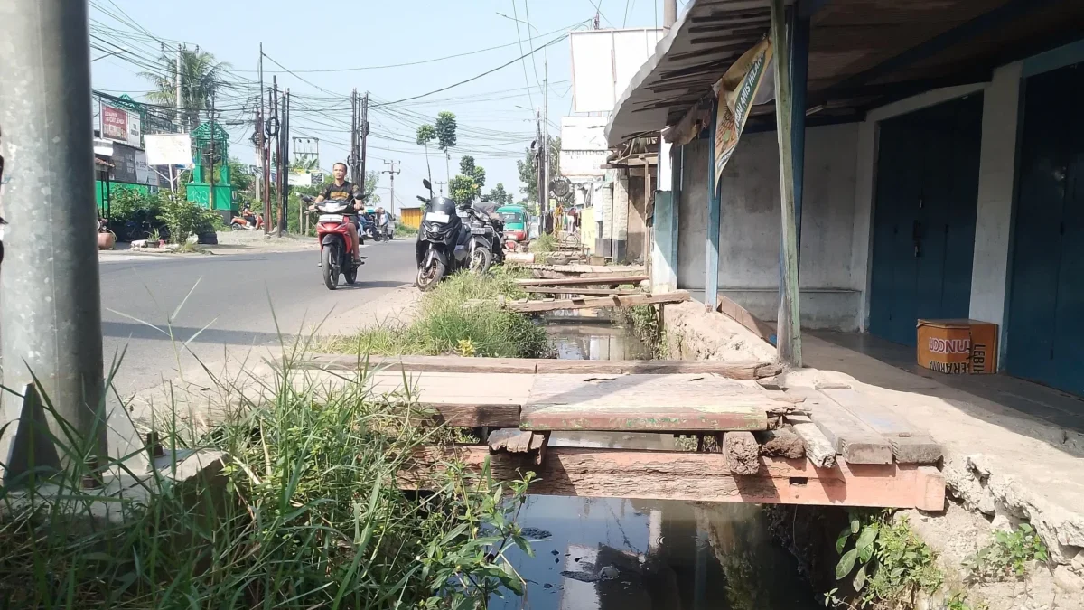 Jembatan darutat dari kayu hasil swadaya warga yang kondisinya kian rapuh, sebab mangkraknya proyek normalisasi drainase DPUTR Kabupaten Bandung di Jalan Raya Rancaekek-Majalaya, wilayah Kampung Rancabatok, RW09 dan RW22, Desa Rancaekekwetan, Kecamatan Rancaekek. (Yanuar/Jabar Ekspres)