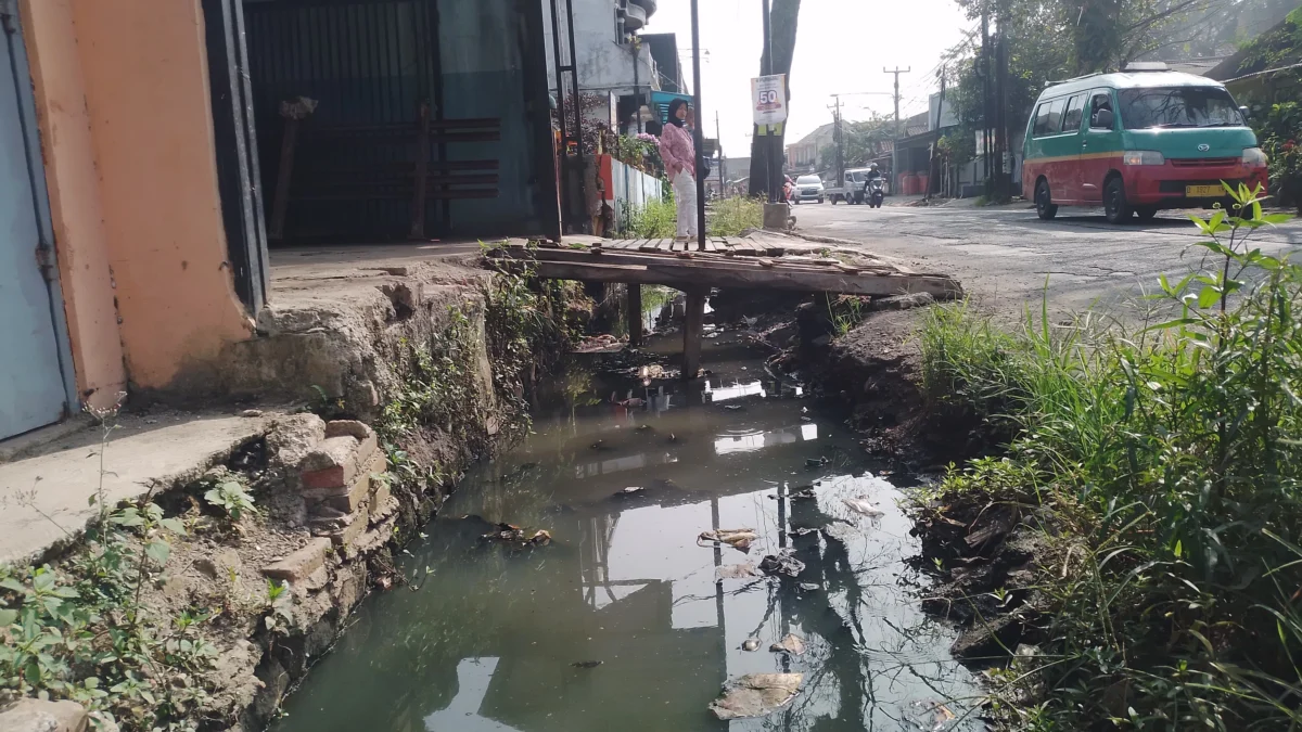 Seorang anak sedang menyebrangi jembatan darutat dari kayu hasil swadaya warga yang kondisinya kian rapuh, sebab mangkraknya proyek normalisasi drainase DPUTR Kabupaten Bandung di Jalan Raya Rancaekek-Majalaya, wilayah Kampung Rancabatok, RW09 dan RW22, Desa Rancaekekwetan, Kecamatan Rancaekek. (Yanuar/Jabar Ekspres)