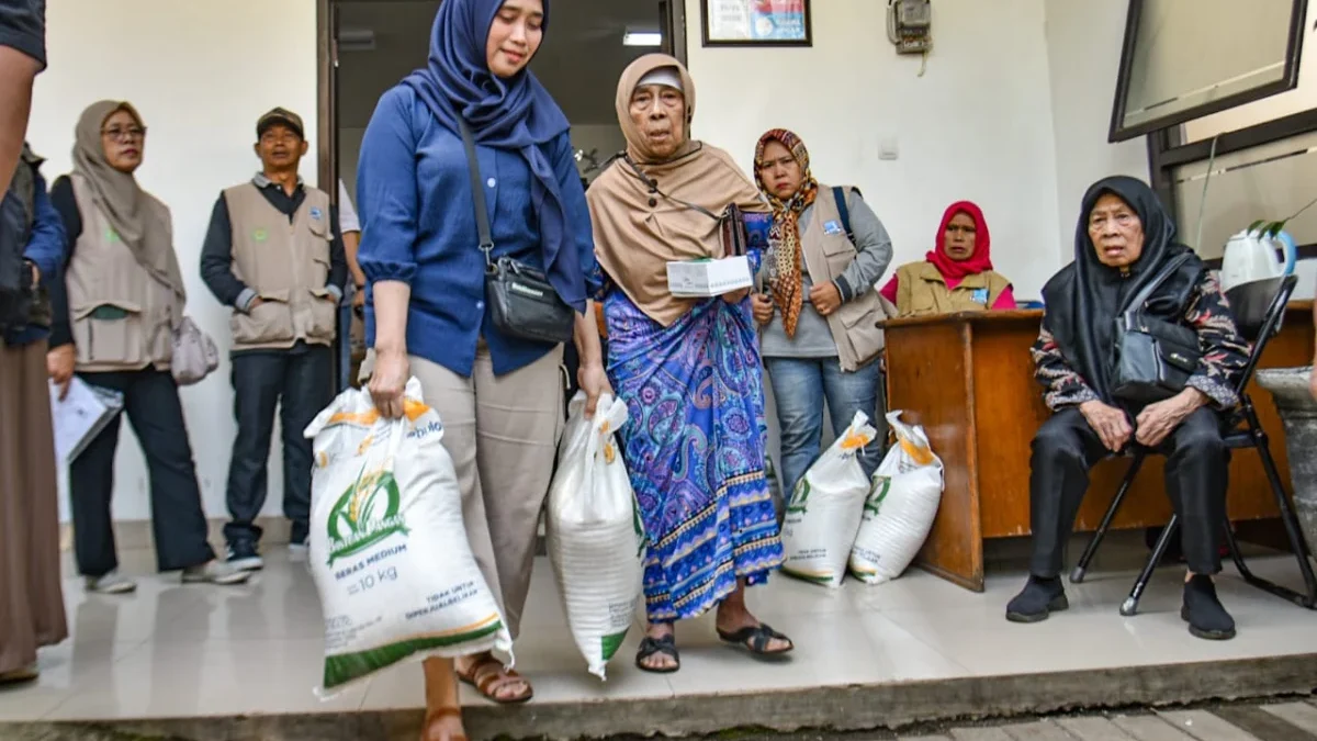 Warga membawa beras saat pendistribusian bantuan cadangan pangan di Kelurahan Cihapit, Kota Bandung, Jumat (18/7). Menurut data Pemerintah Kota Bandung menyalurkan bantuan cadangan pangan dari Badan Pangan Nasional (Bapanas) berupa 10 kilogram beras kepada 85.167 warga di 151 yang ada kelurahan di Kota Bandung. Foto: Dimas Rachmatsyah / Jabar Ekspres