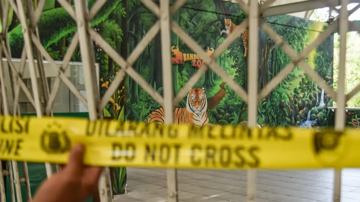 Petugas kepolisian memegang garis polisi yang terpasang di gerbang masuk Kebun Bintang Bandung yang ditutup di