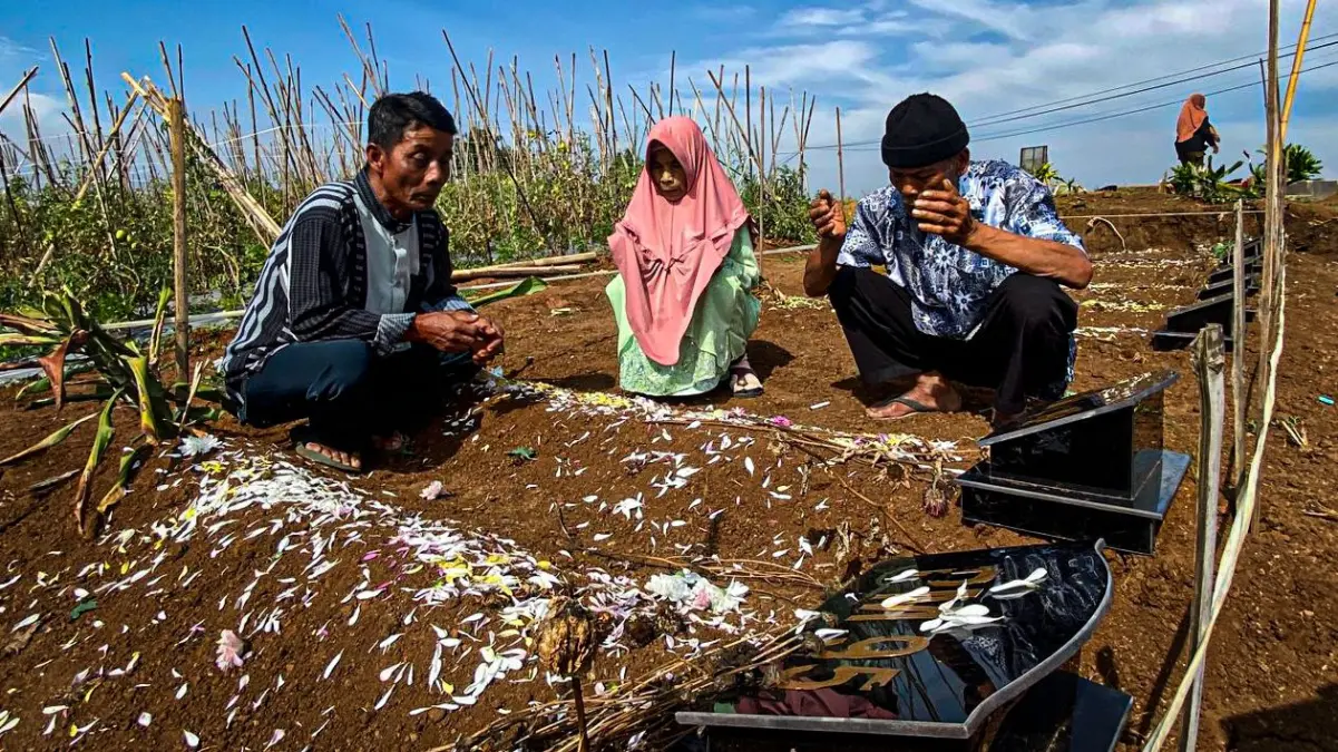 Eha (41) menundukkan kepala di hadapan pusara keluarganya di TPU Kampung Barunyatuh, Desa Pasirlangu, Kecamata
