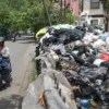 Pengendara sepeda motor melintas di samping tumpukan sampah yang belum diangkut di TPS Jalan Guntursari Wetan,