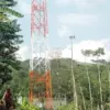Seorang lansia tengah berjalan kaki sambil menarik gerobak melintasi menara BTS yang berdiri tegak di Dusun Le