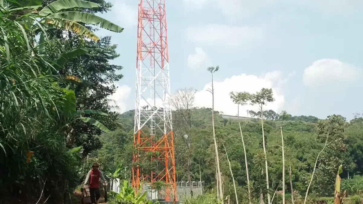 Seorang lansia tengah berjalan kaki sambil menarik gerobak melintasi menara BTS yang berdiri tegak di Dusun Le