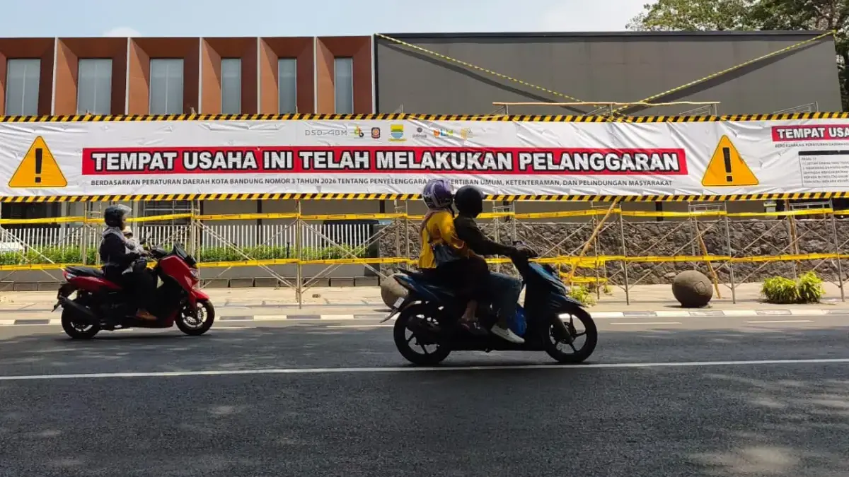 Warga menggunakan sepeda motor melintas di depan garis segel Satpol PP terkait kasus penebangan pohon tanpa iz