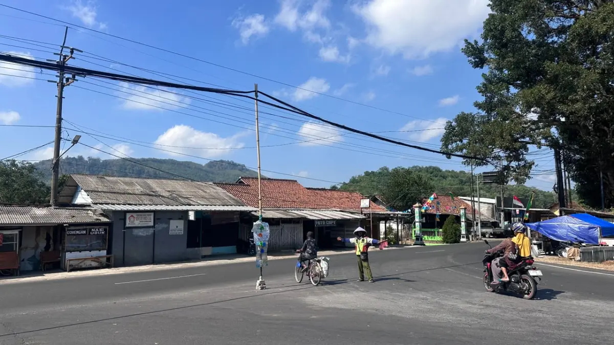 Relawan pengatur lalu lintas kendaraan berdiri di dekat tiang bambu yang digunakan untuk menopang kabel intern