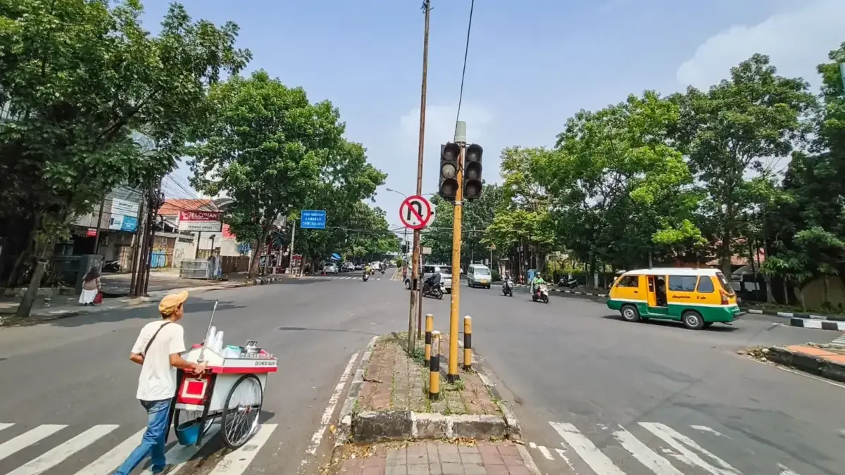 Pedagang cincau menyeberang jalan di samping Alat Pemberi Isyarat Lalu Lintas (APILL) yang tidak berfungsi di