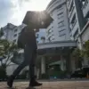 Pekerja mengenakan payung saat melintas di perkantoran Jalan Dr, Djunjunan, Kota Bandung, Rabu (21/10/2026). B