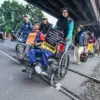 Penyandang disabilitas berjalan dengan kursi roda menyeberangi perlintasan jalur kereta api sebidang di Jalan