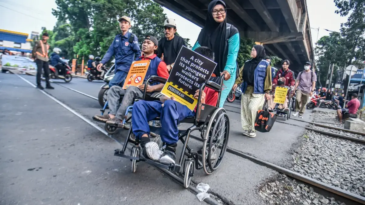 Penyandang disabilitas berjalan dengan kursi roda menyeberangi perlintasan jalur kereta api sebidang di Jalan