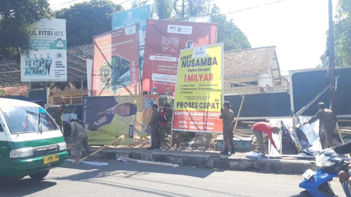 Petugas Satpol PP Garut saat menertibkan baligo bacalon bupati dan reklame yang terpasang percis dirembok SMPN