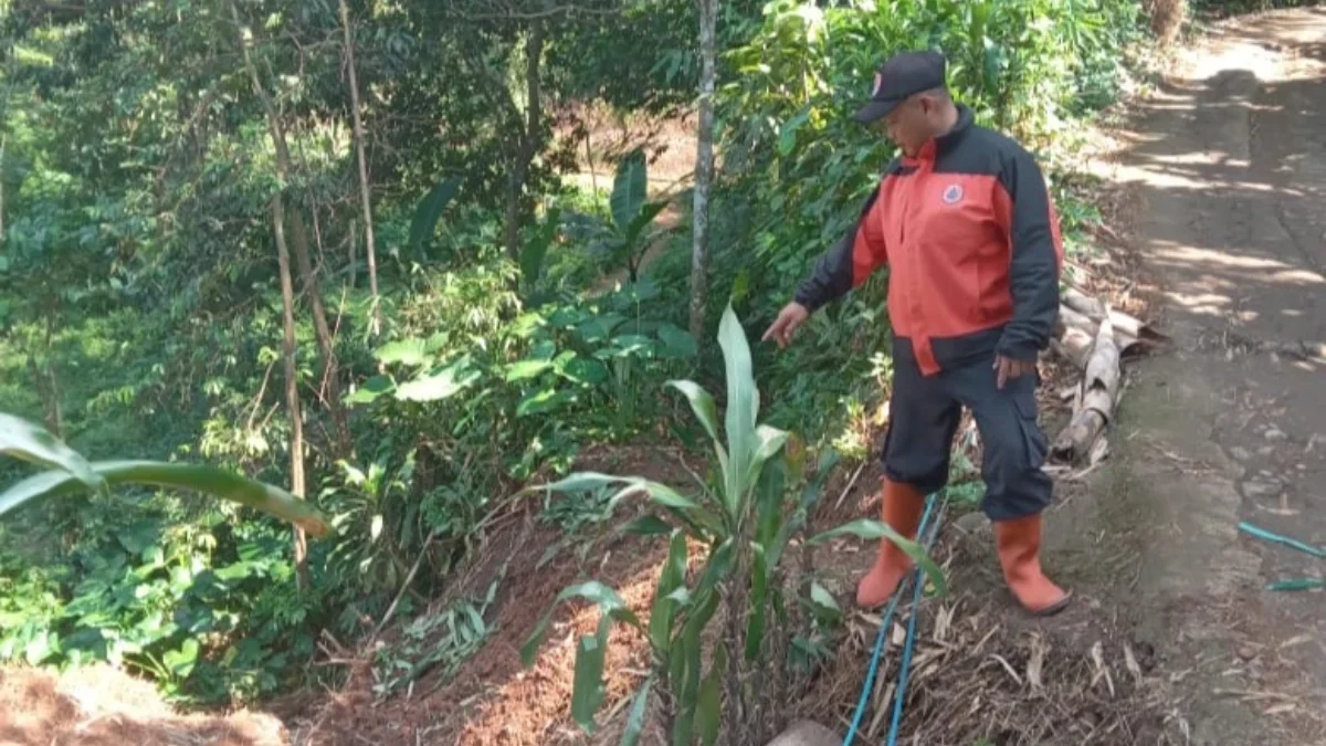 Salah seorang warga saat menunjukan lokasi longsor yang mengakibatkan jalan lingkungan rusak