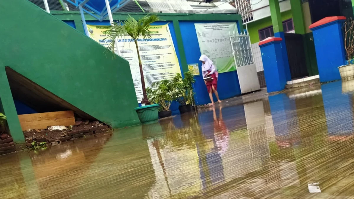 MENGGENANG: Para siswa dan guru terpaksa membuka alas kaki saat akan masuk sekolah karena pintu gerbangnya terendam air, di halaman Gedung Sekolah Dasar Negri (SDN) Parakanmuncang 2, Desa Sindangpakuon, Kecamatan Cimanggung, kemarin