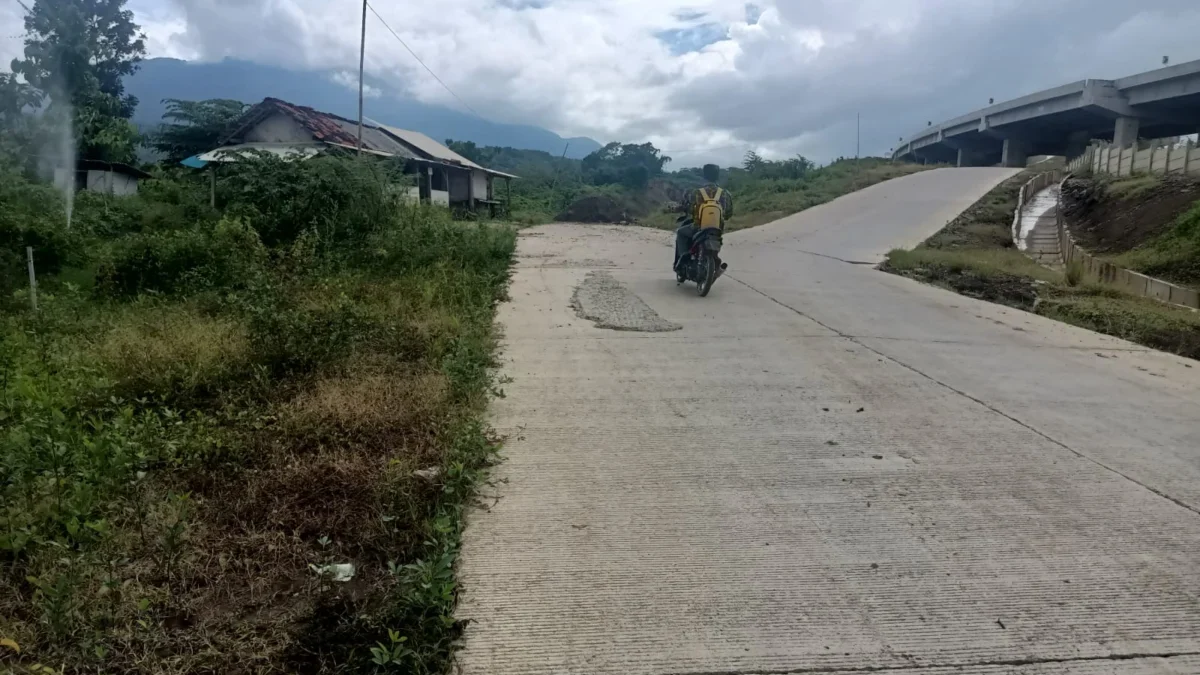 BERBAHAYA: Seorang pengendara motor saat melintas di jalan yang terkena longsor wilayah bawah Jembatan Tol Kad