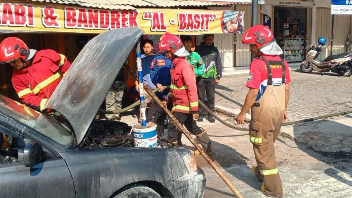 HANGUS: Petugas pemadam kebakaran saat berusaha memadamkan api di mobil sedan yang terbakar di Desa Rancamulya