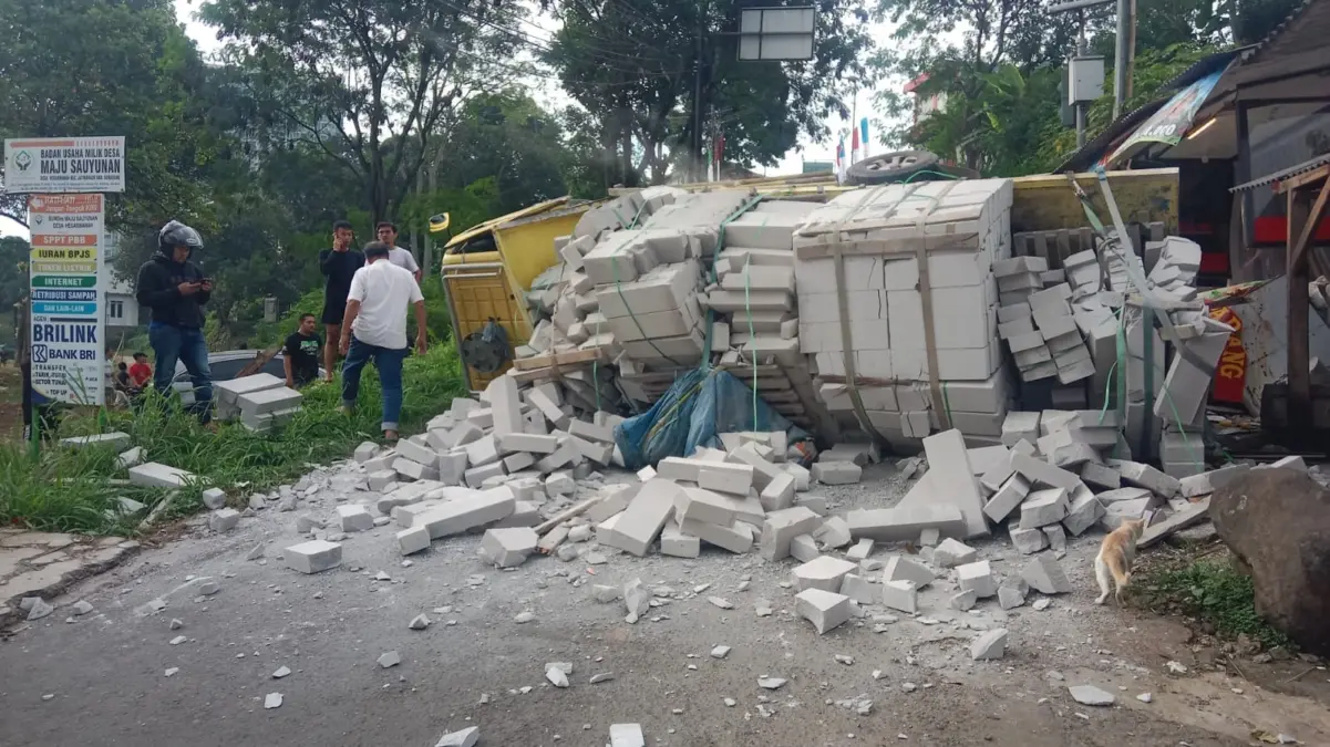 KECELAKAAN: Truk bermuatan bata ringan terguling saat melintasi tanjakan curam di Jalan Cikuda–Cilayung, Desa