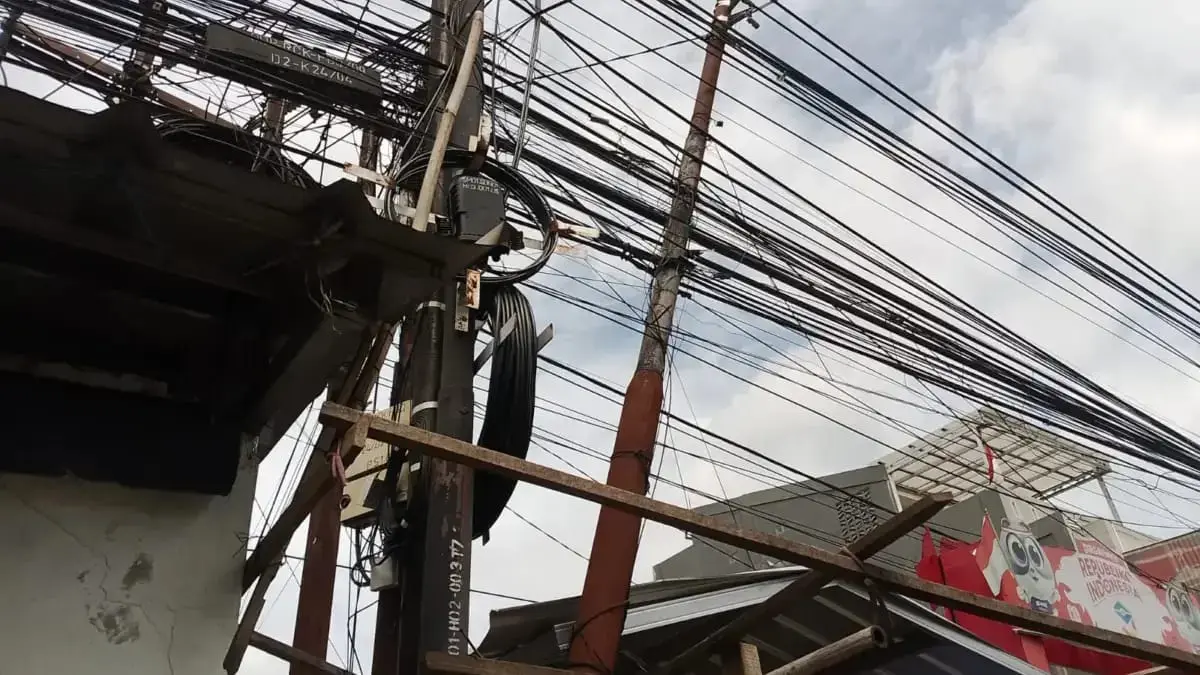 Ilustrasi - Kabel utilitas yang menjuntai dan saling silang di kawasan perkotaan, mencerminkan lemahnya penata