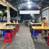 Suasana warung kopi pada malam hari dengan meja dan kursi untuk pengunjung.